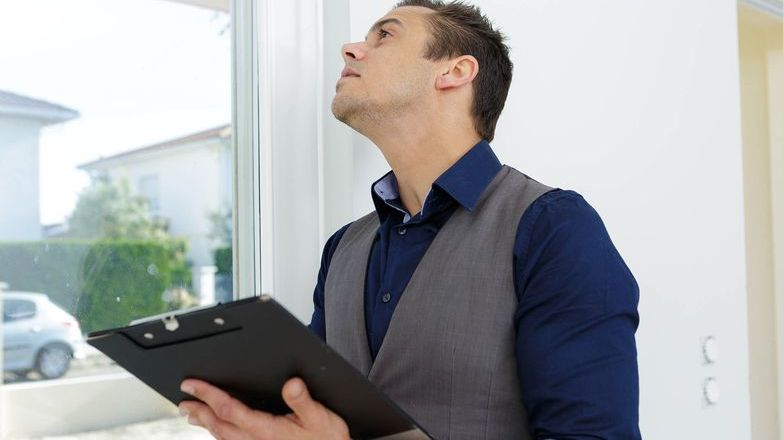 Man holding a clipboard and inspecting the windows of a property