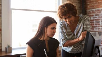 Apprentice at computer getting guidance from trainer